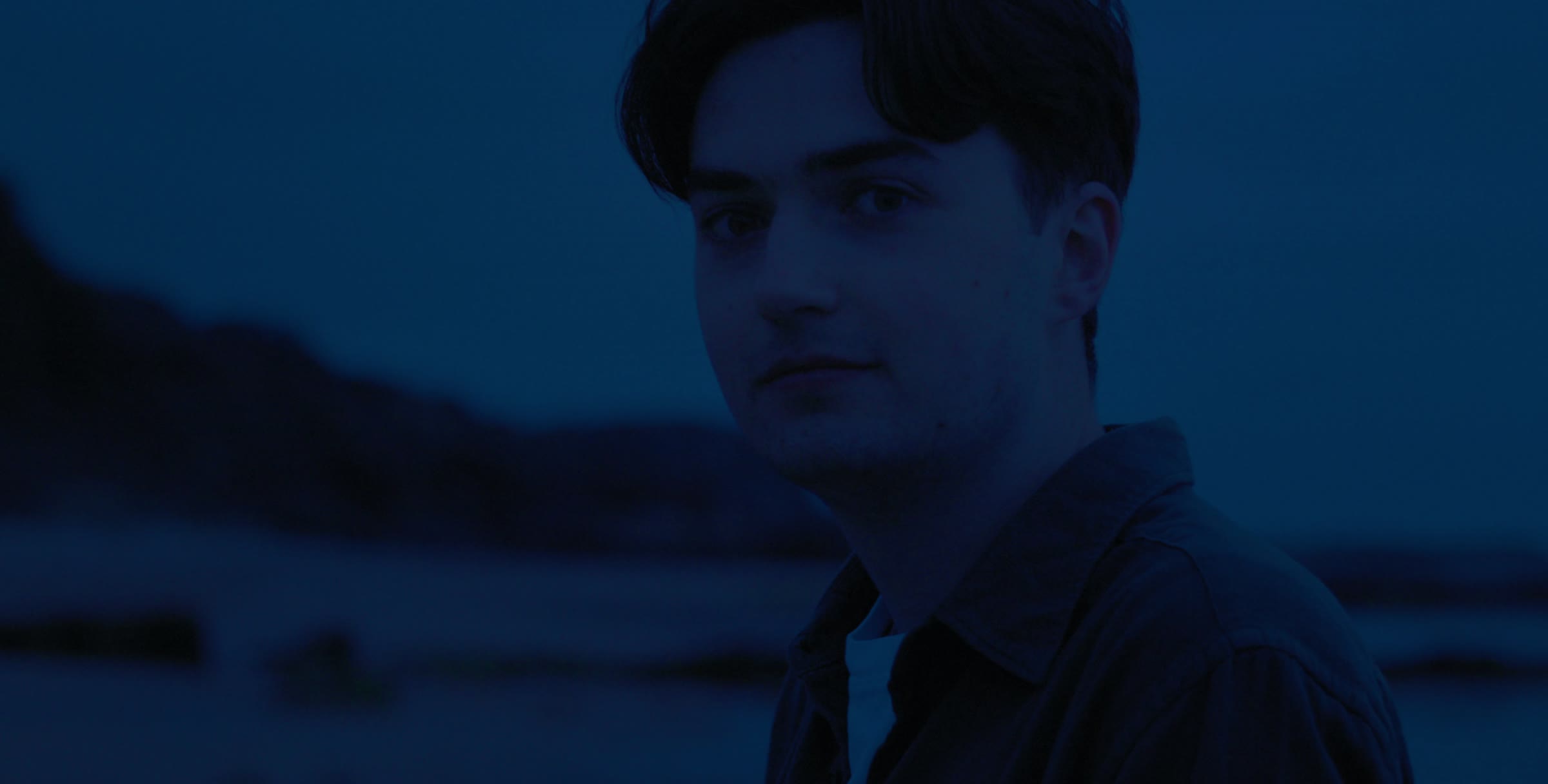 A boy in blue evening light by the sea
