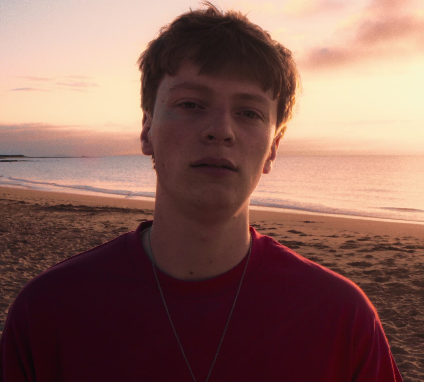 A boy in a red t-shirt on the beach at sunset