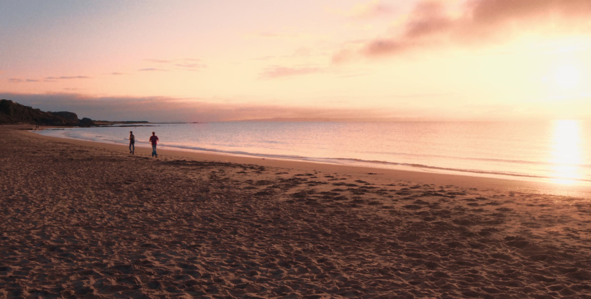 Two figures on a wide beach at sunset